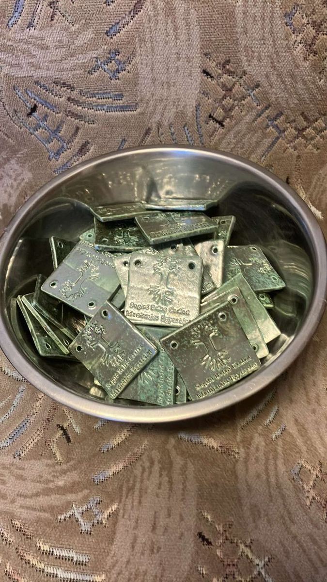 Tálban sorakozó, zöld mázas kerámialapok az egyesület életfa-emblémájával.