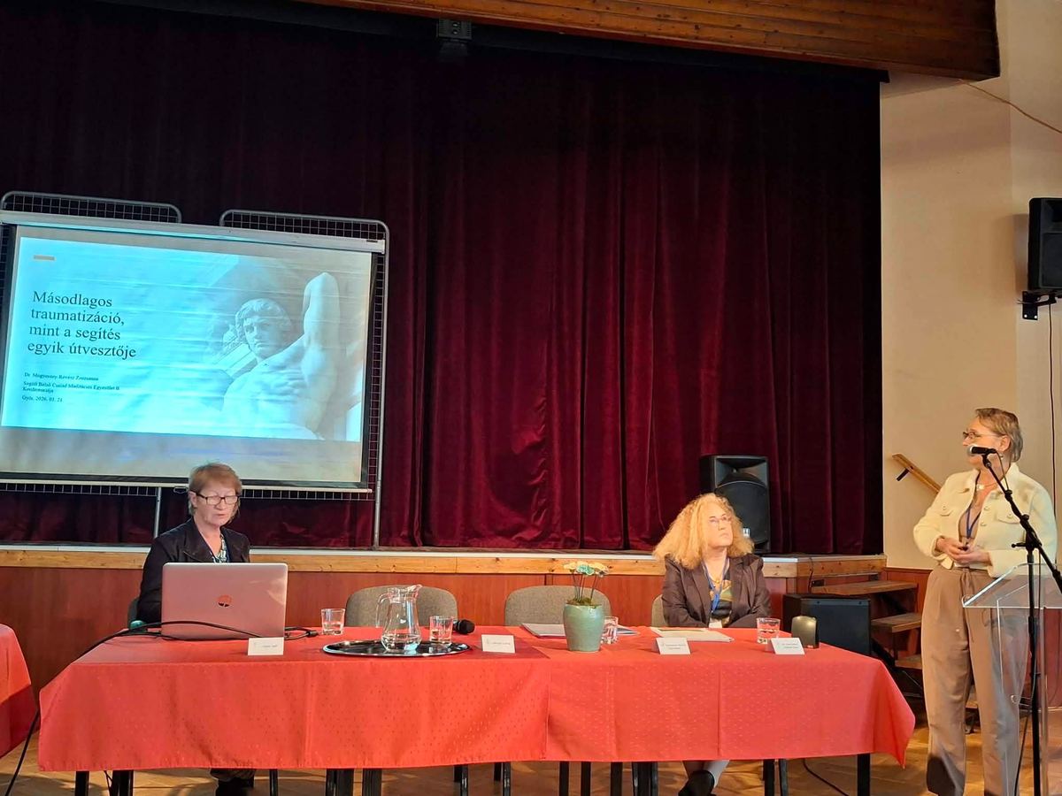 Előadás a színpadon, a vetítővásznon a „Másodlagos traumatizáció, mint a segítés egyik útvesztője” című dia.